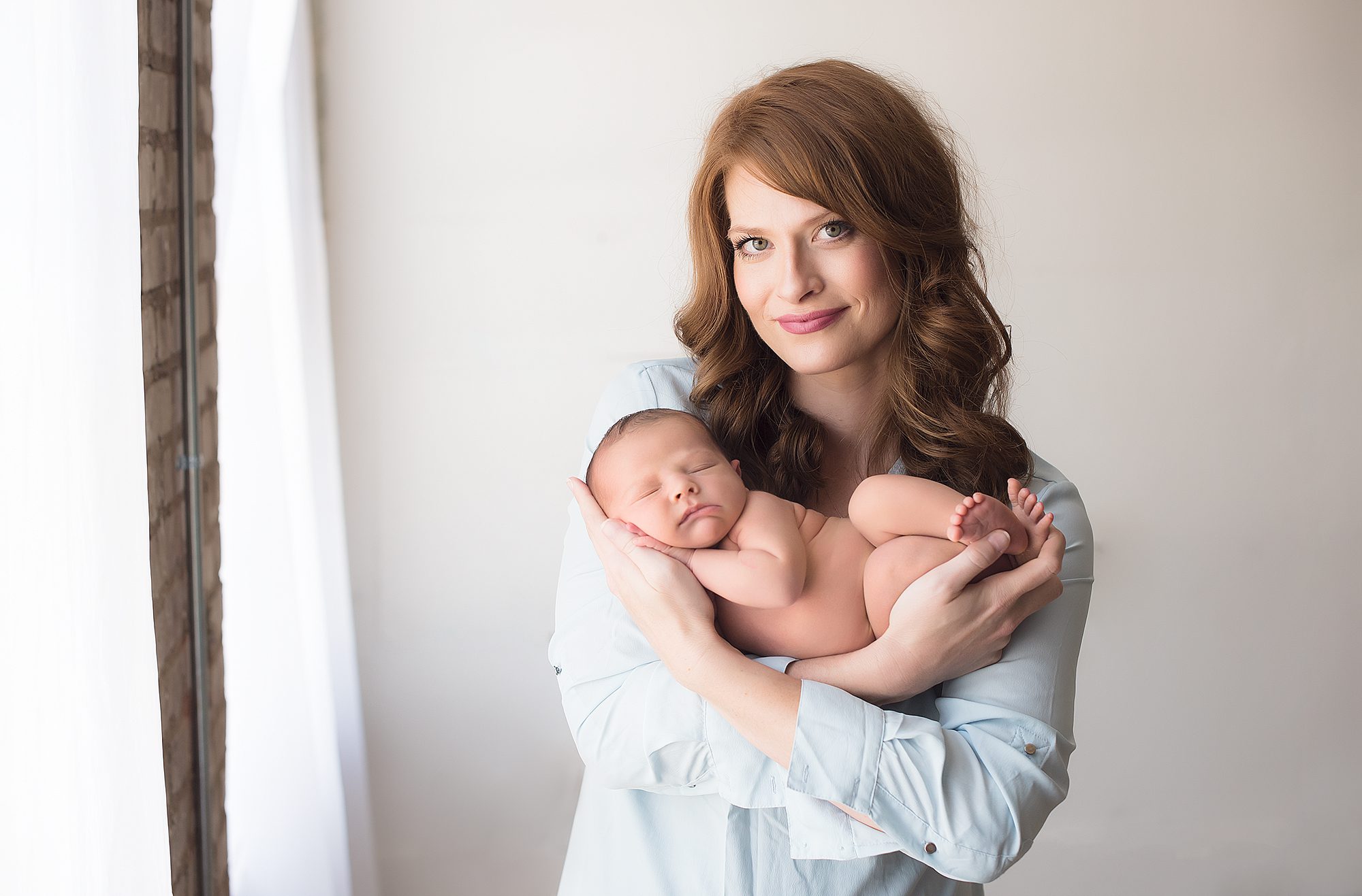 redheaded mom wearing a blue shirt and holding newborn baby boy