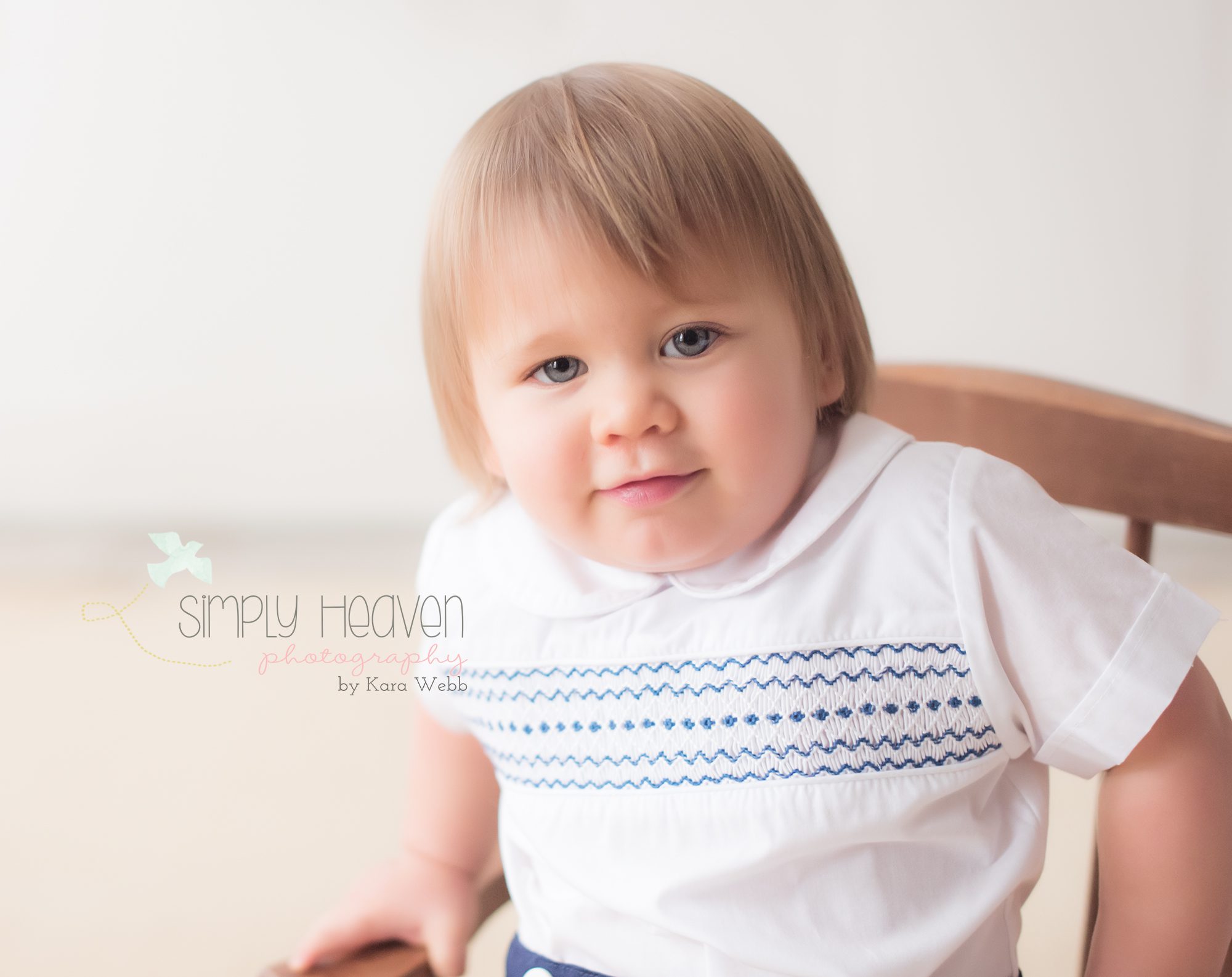 toddler boy with blue eyes and peter pan collared shirt sitting in a rocking chair