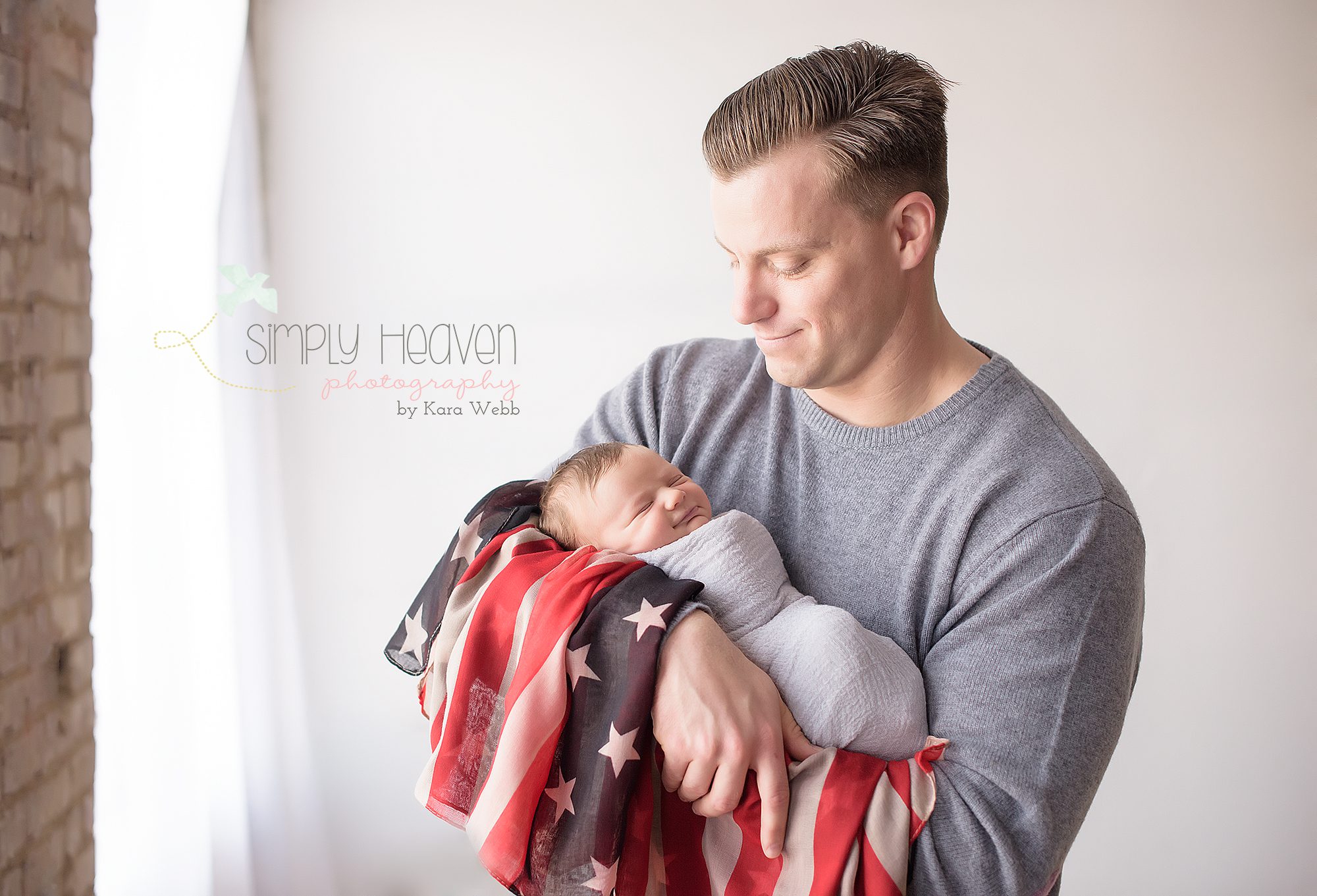 dad holding and looking at newborn baby boy while wrapped in a flag