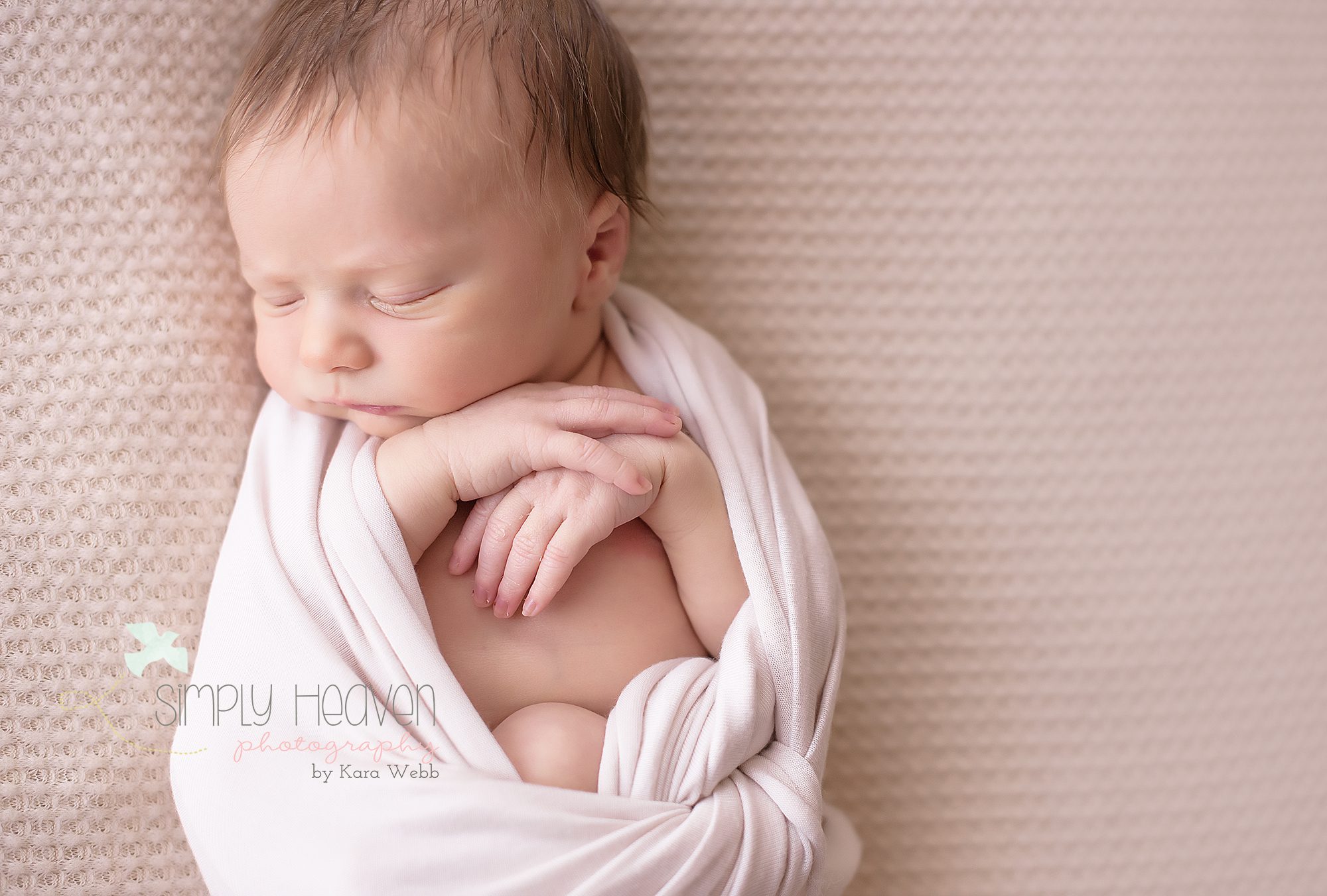 Newborn baby boy wrapped in a beige cloth so that his hands are showing.