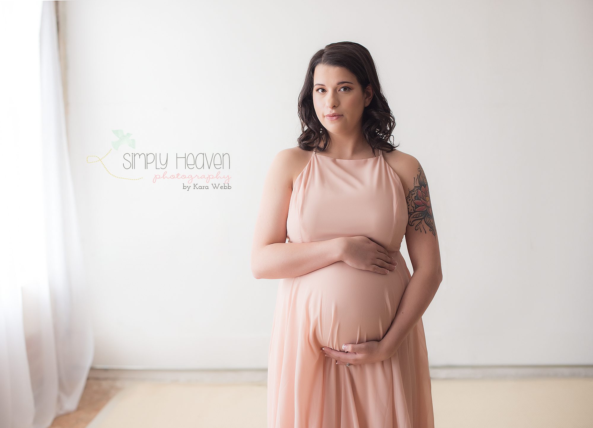 maternity pictures of a lady in a pink dress in front of a white wall