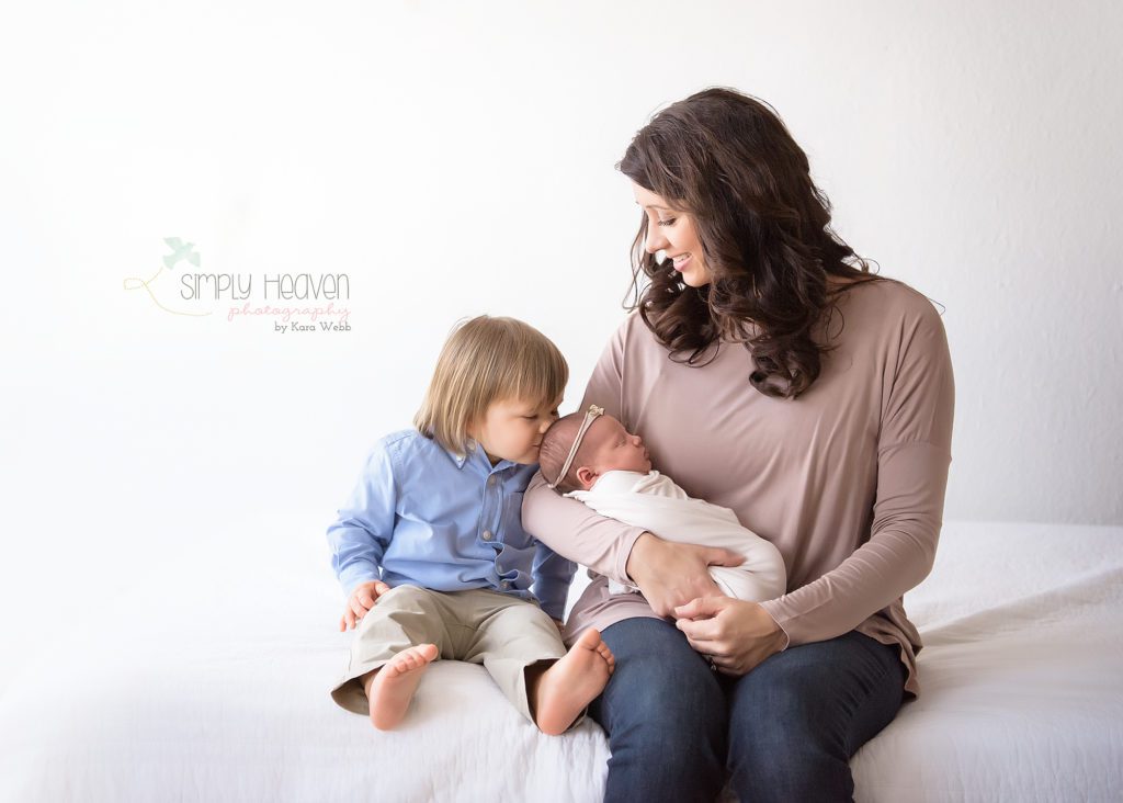 mom, brother, and new sister sitting on a white couch, brother kissing sister