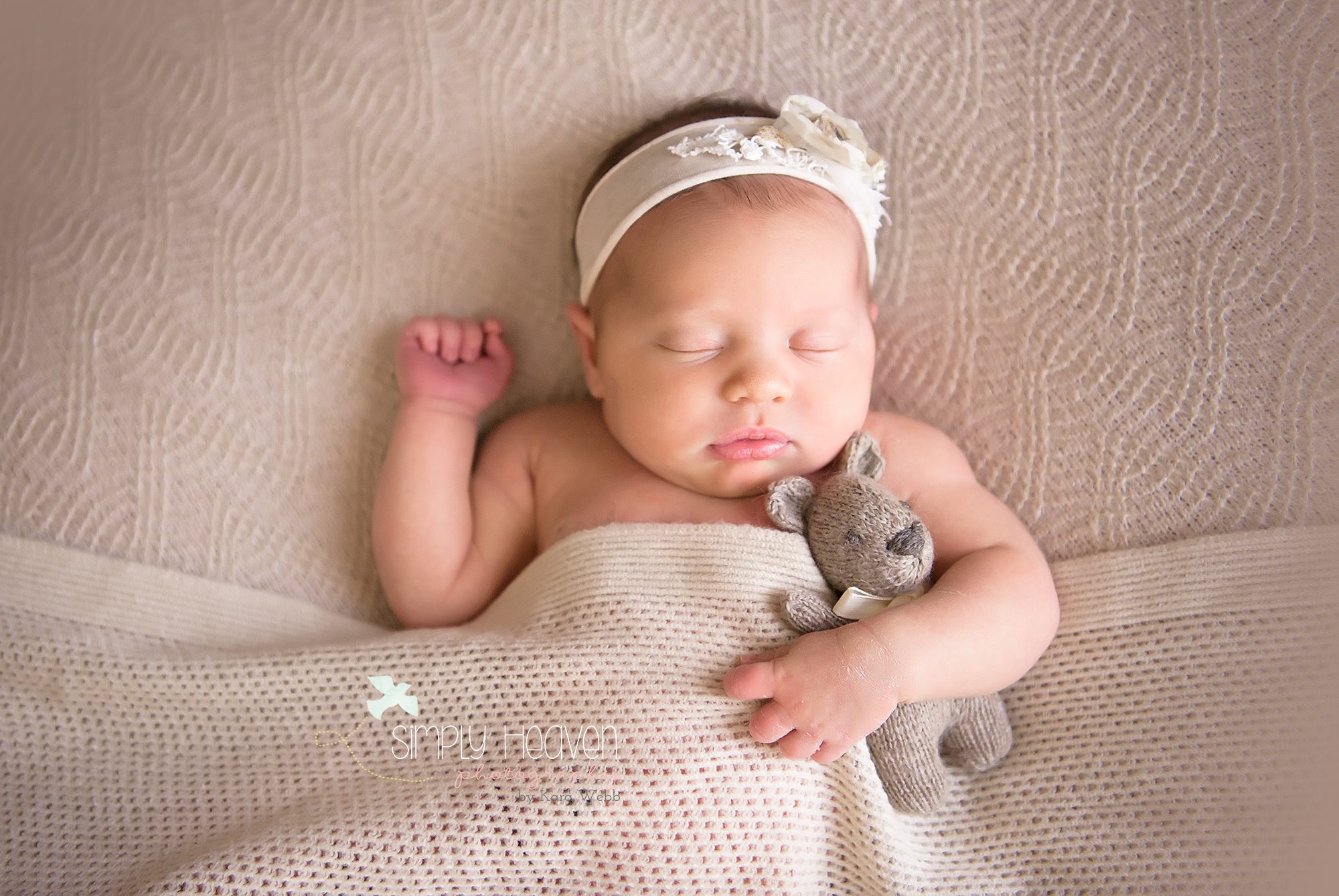 newborn baby girl holding a teddy bear with a cream headband