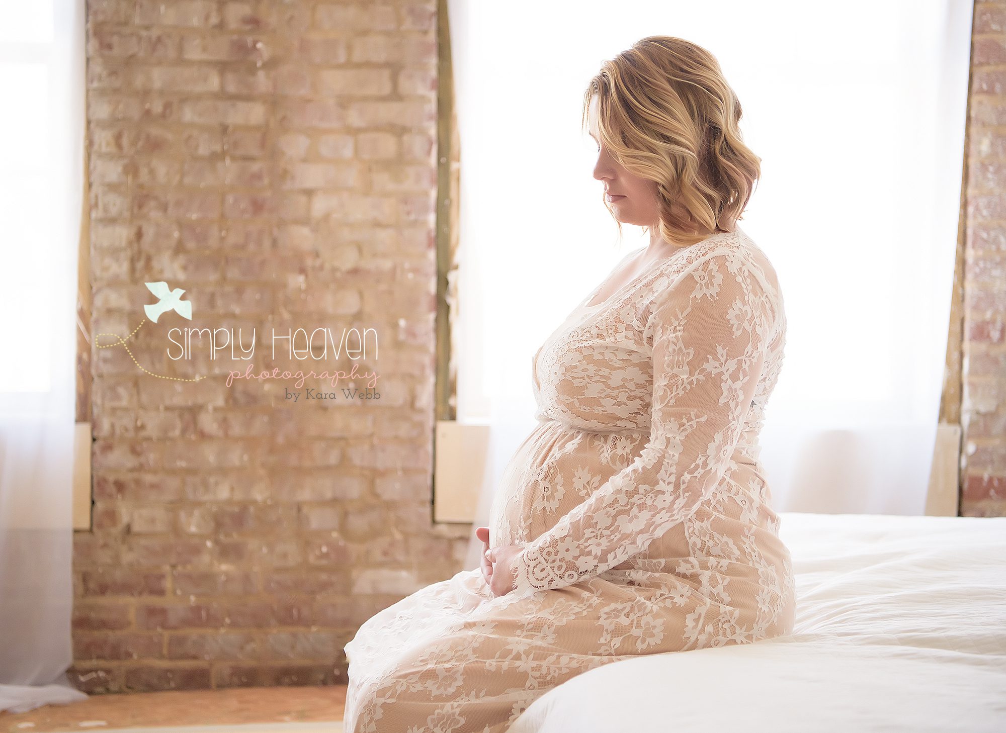 maternity portrait of mom sitting on bed in front of a window