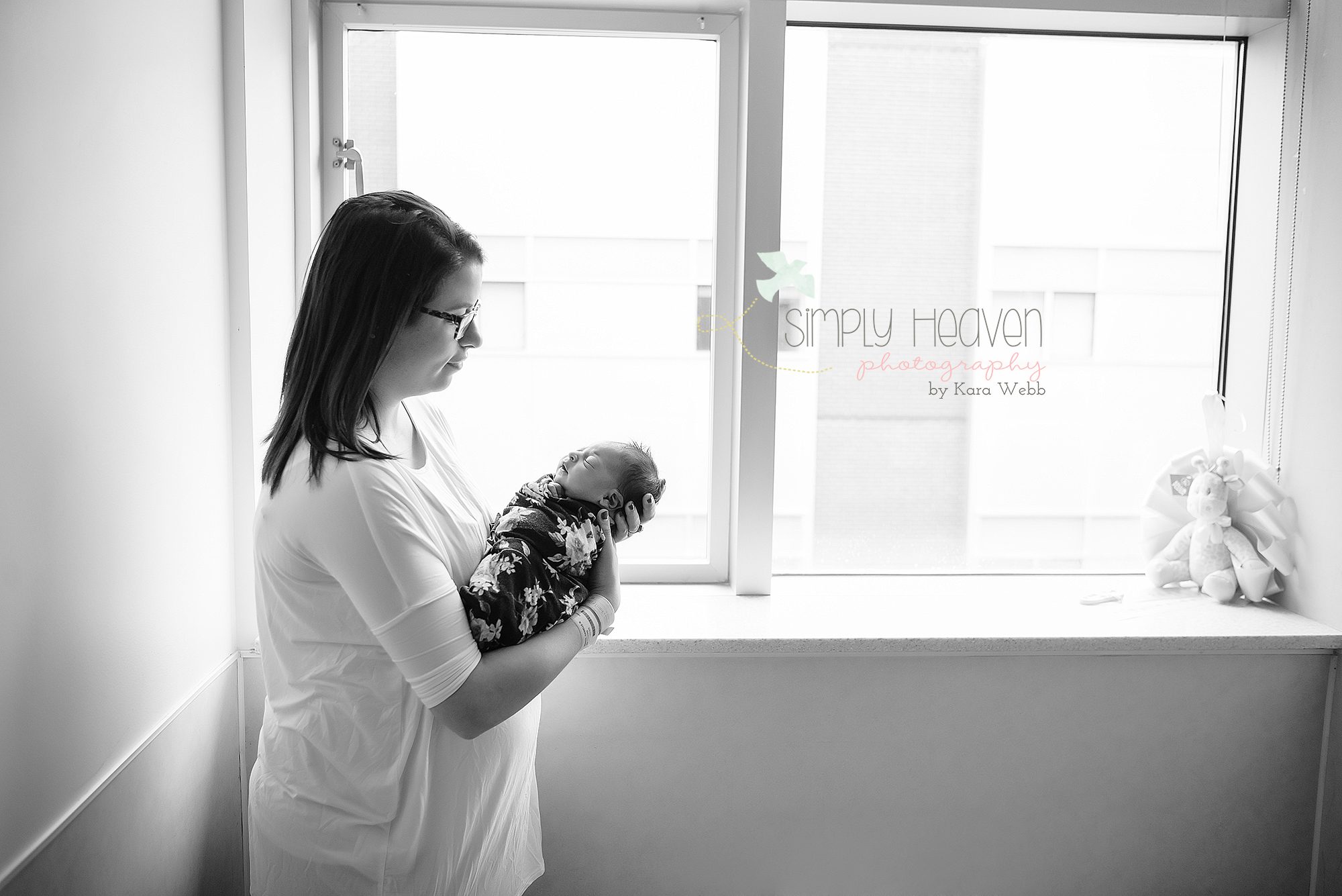 mom holding her swaddled newborn baby girl in front of a hospital window