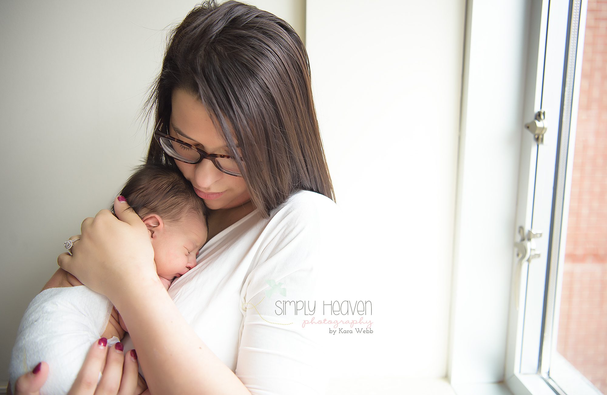 mom holding her newborn baby girl in front of a hospital window