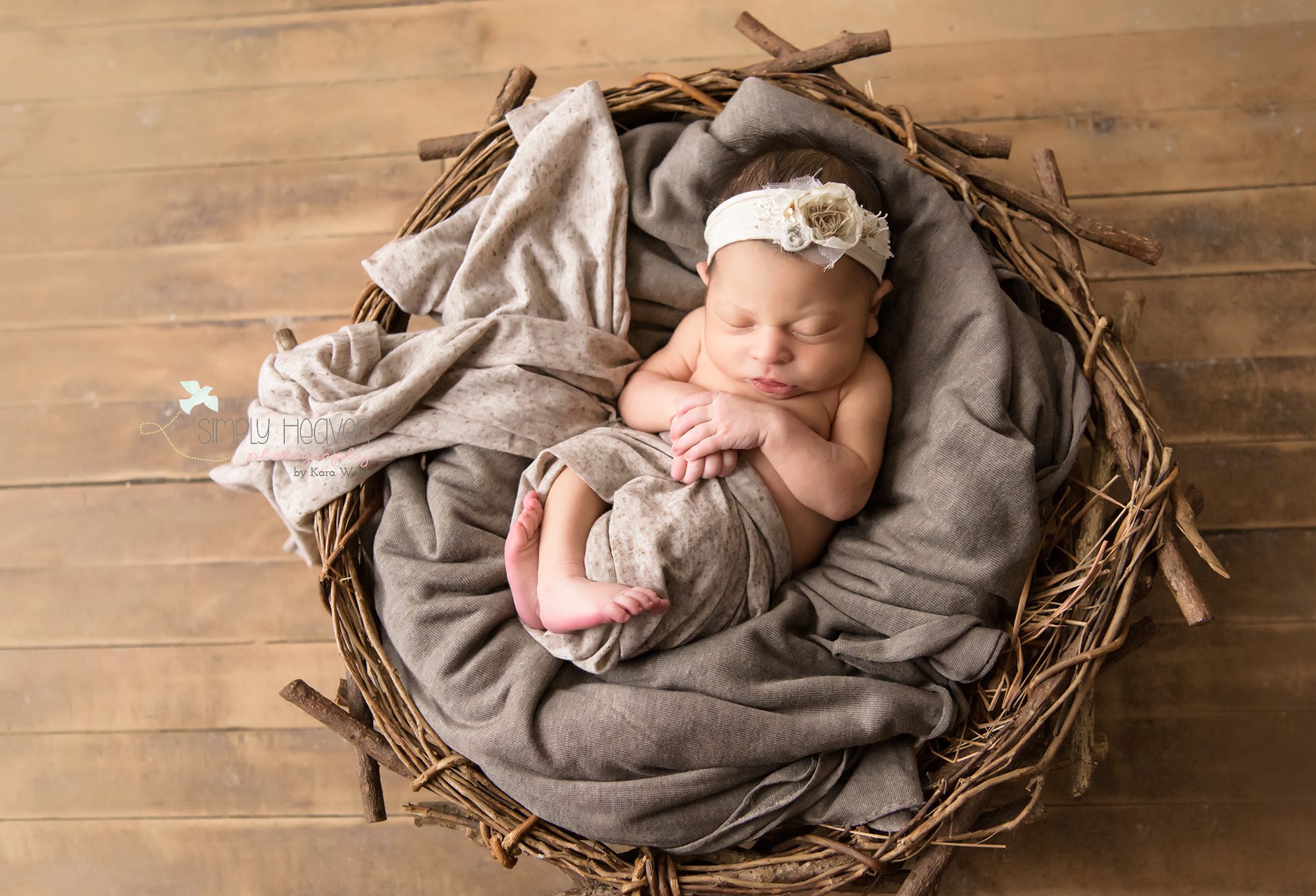 newborn baby girl with a white headband swaddled in a nest