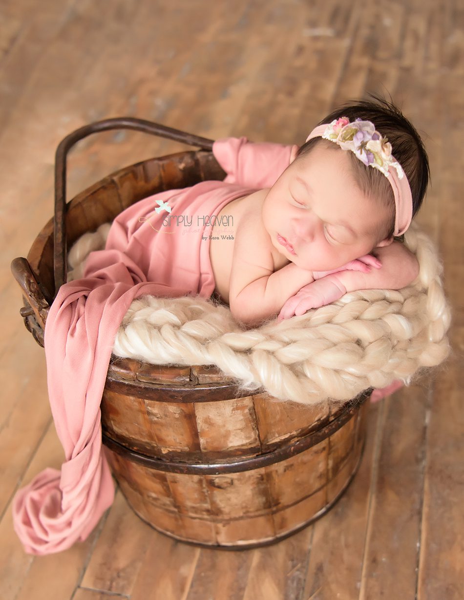newborn baby girl in a bucket with a floral pink headband