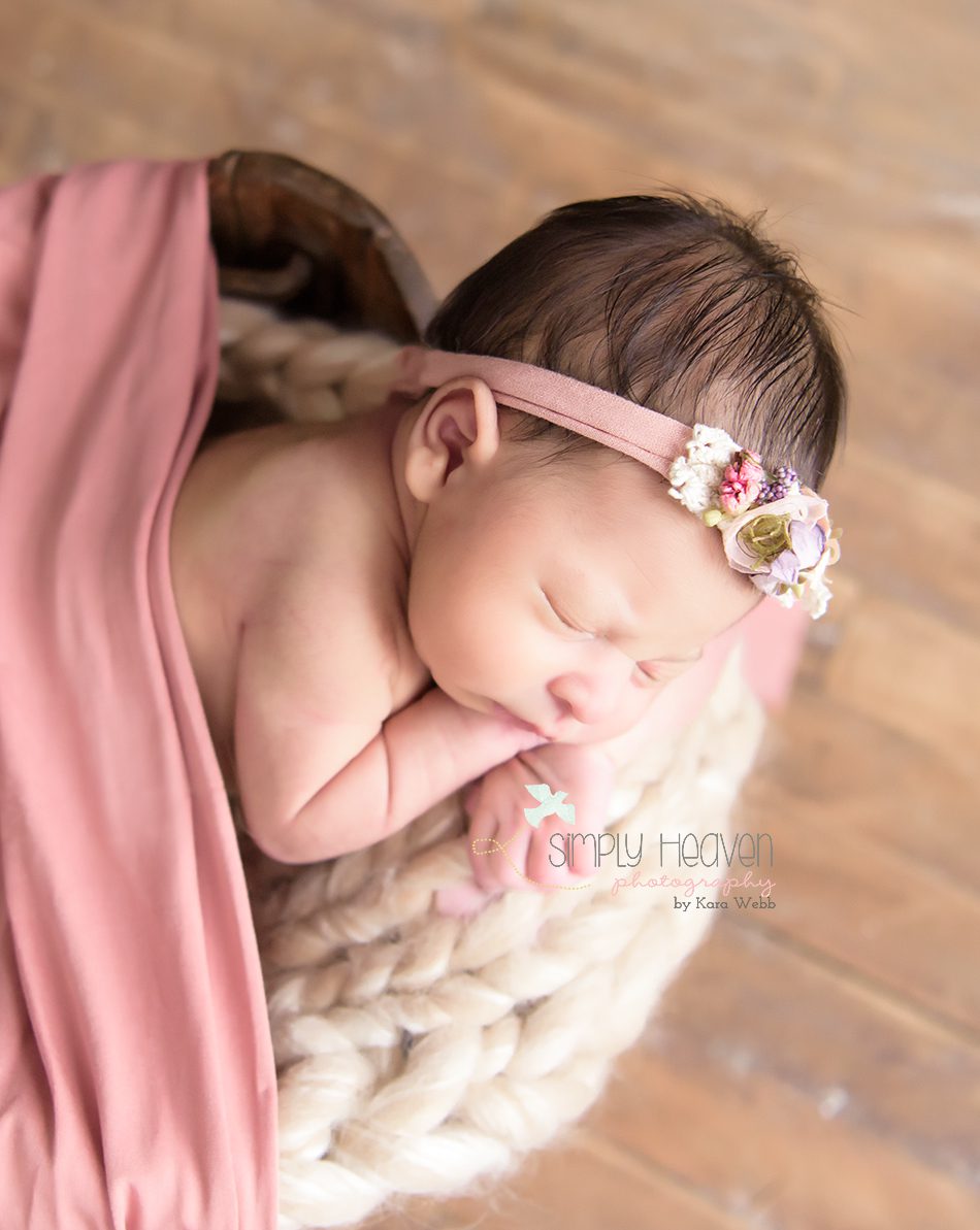 newborn baby girl in a bucket with a pink headband