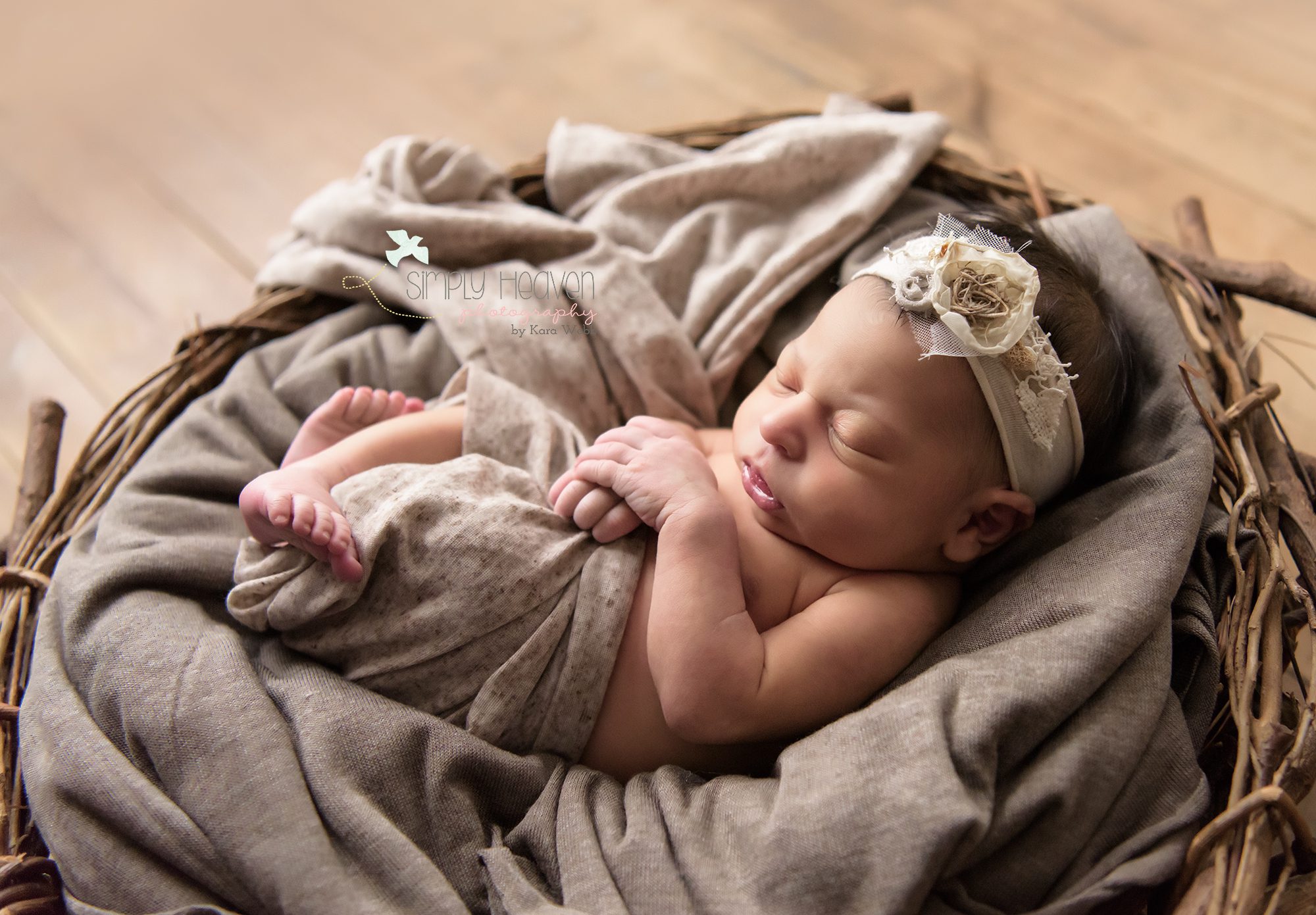 newborn baby girl with a white headband swaddled in a nest layed on the ground