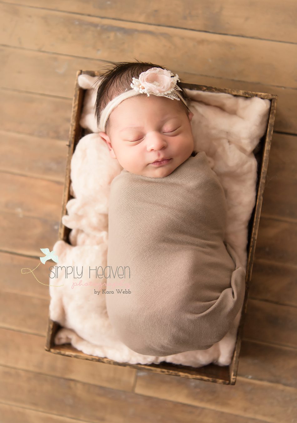 studio newborn photography session of a newborn baby girl swaddled in a fawn color in a box with a pink headband 