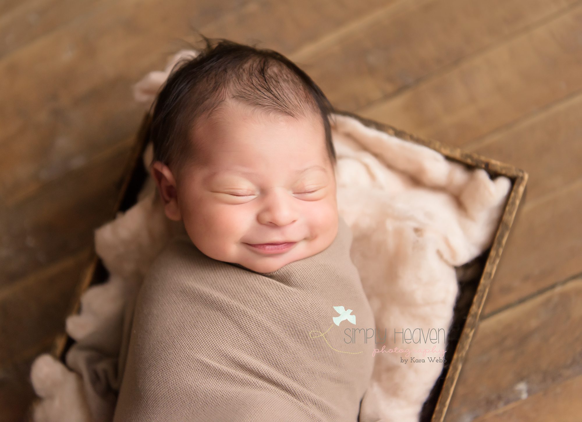 Smiling newborn baby girl swaddled in a fawn color in a box