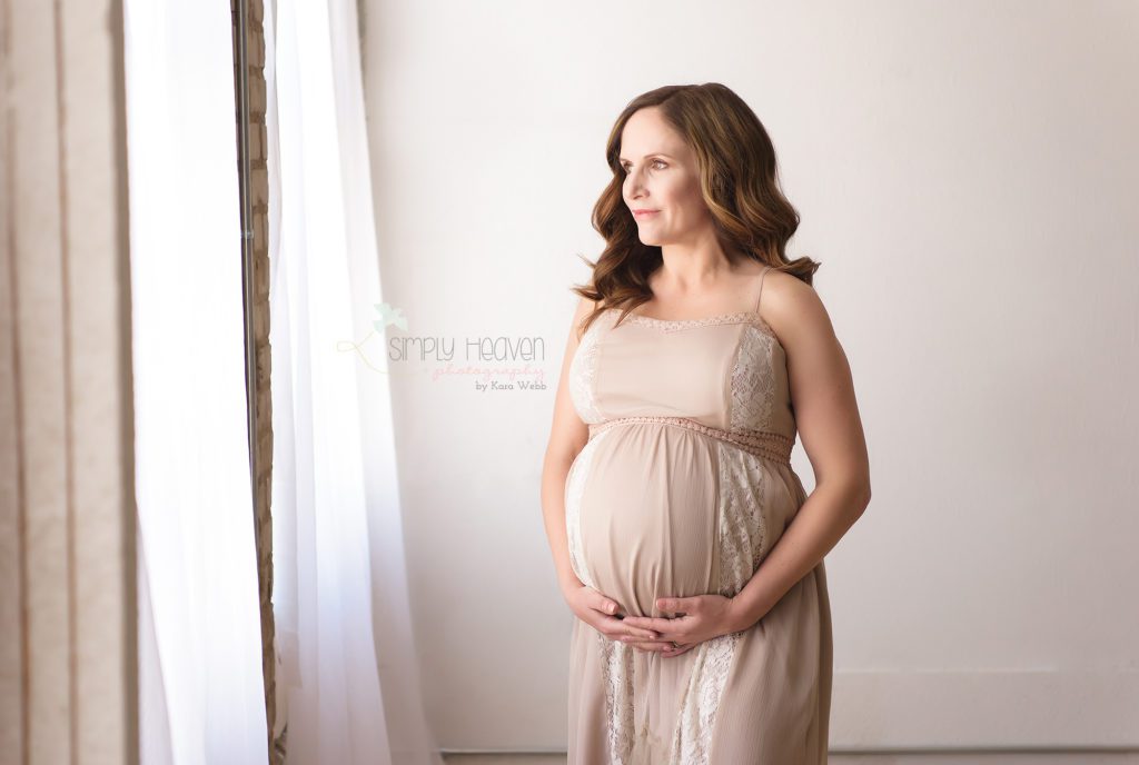 pregnant woman standing in front of a window during a maternity portrait session