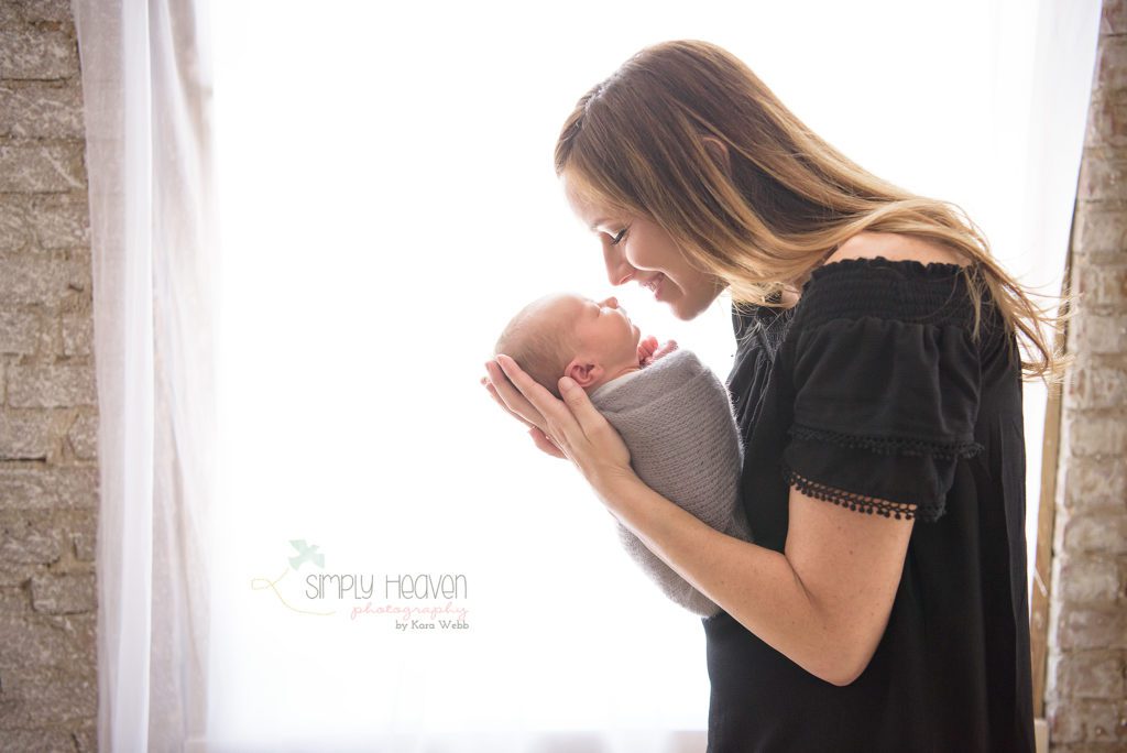 mom holding a newborn baby boy in front of a window